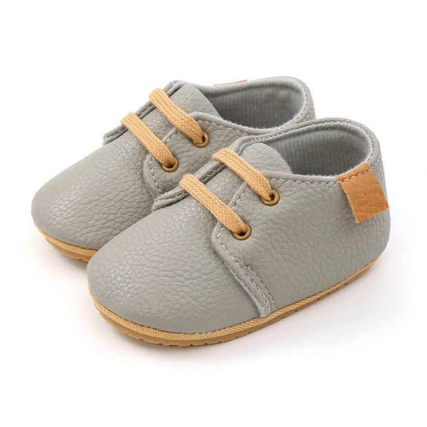 Pair of gray baby shoes with tan laces and soles on a white background