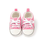 Pair of pink baby sneakers with white laces on a white background