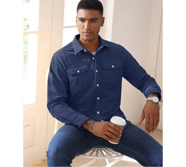 Man wearing a blue denim shirt and jeans, holding a coffee cup indoors.