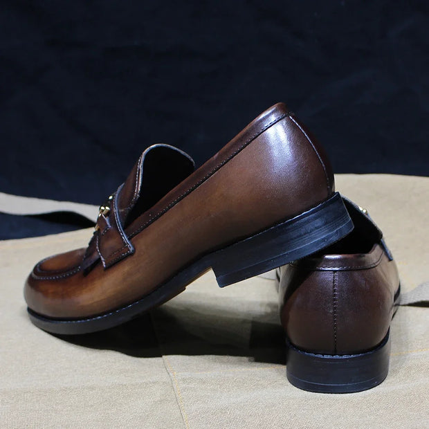 Pair of brown leather loafers on a textured surface with a dark background