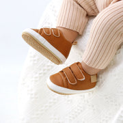 Children's feet wearing brown shoes with white soles on a white surface