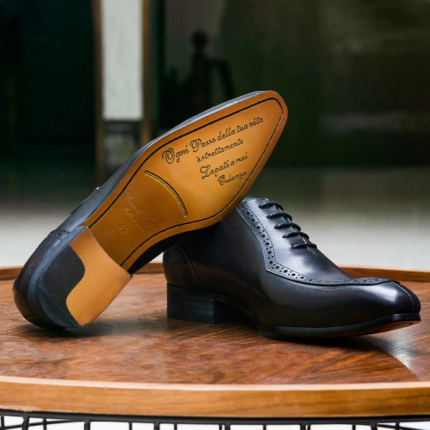 Black dress shoes with brown soles on a wooden surface