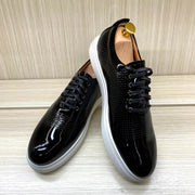 Black patent leather shoes with white soles on a light wooden floor.