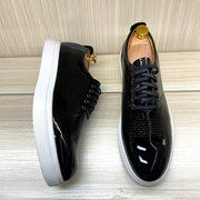 Black patent leather shoes with white soles on a wooden surface