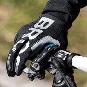 Close-up of a person wearing black gloves with a brand logo, holding bicycle handlebars.