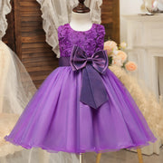 Purple flower girl dress with a large bow on a mannequin against a decorative background.