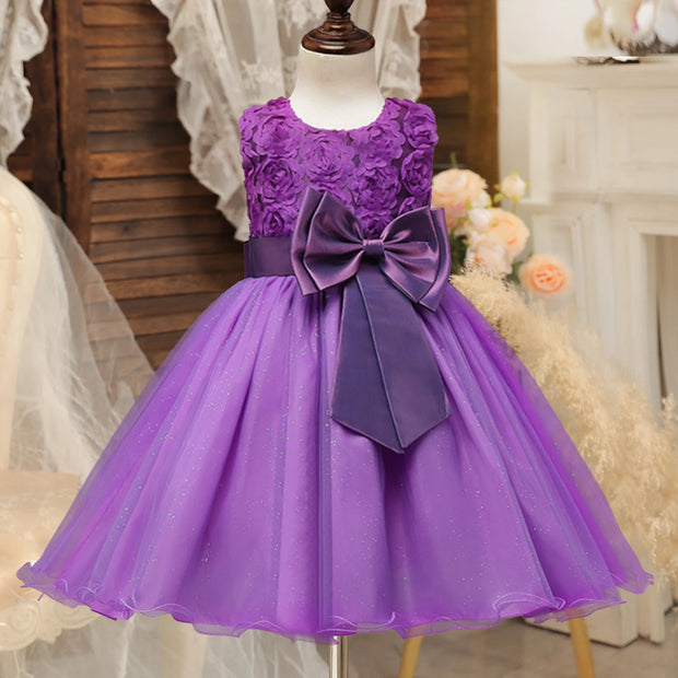 Purple flower girl dress with a large bow on a mannequin against a decorative background.