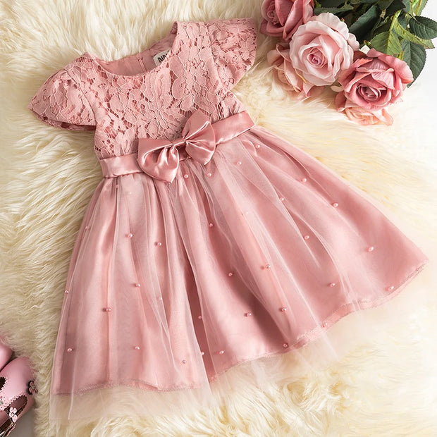 Pink lace dress with a bow on a fluffy white surface with pink roses.