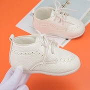 White baby shoes on a white surface with an orange background