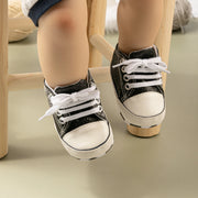 Black and white sneakers worn by a child on a wooden stool.