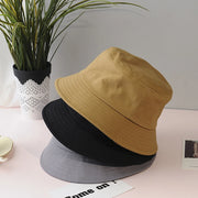 Three bucket hats in black, beige, and gray on a surface with a plant in the background.
