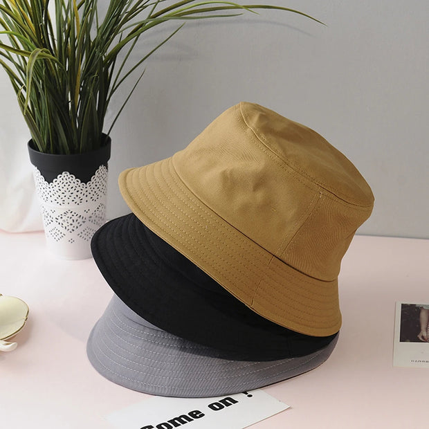 Three bucket hats in black, beige, and gray on a surface with a plant in the background.