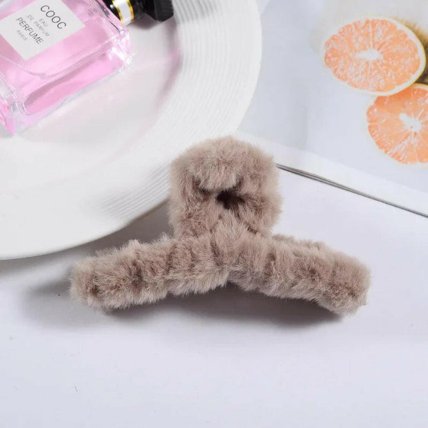 Fluffy brown hanger on a white surface with a pink perfume bottle and orange slices in the background.