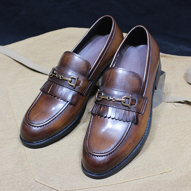 Pair of brown leather loafers with decorative straps on a beige surface.