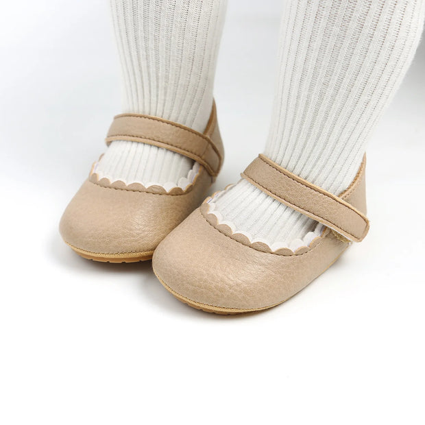 Beige baby shoes with white socks on a light gray background