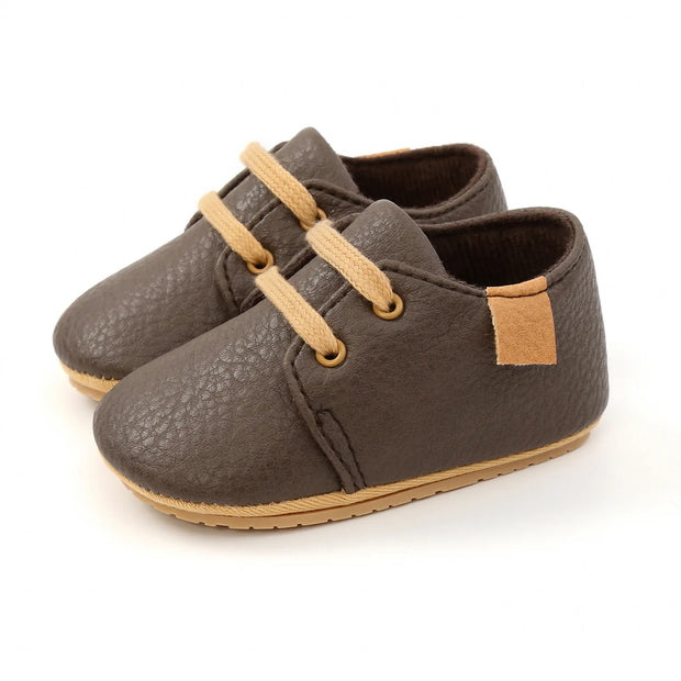 Pair of brown baby shoes with tan laces on a white background