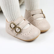 Beige baby shoes with gold buckles worn by a child on a white background