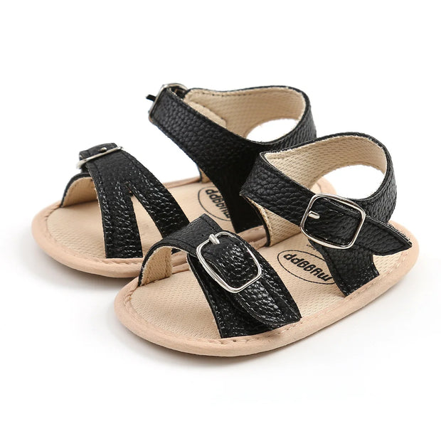 Pair of black and beige baby sandals with buckles on a white background