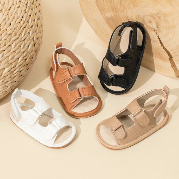Four pairs of children's sandals in different colors on a beige surface with a woven basket in the background.