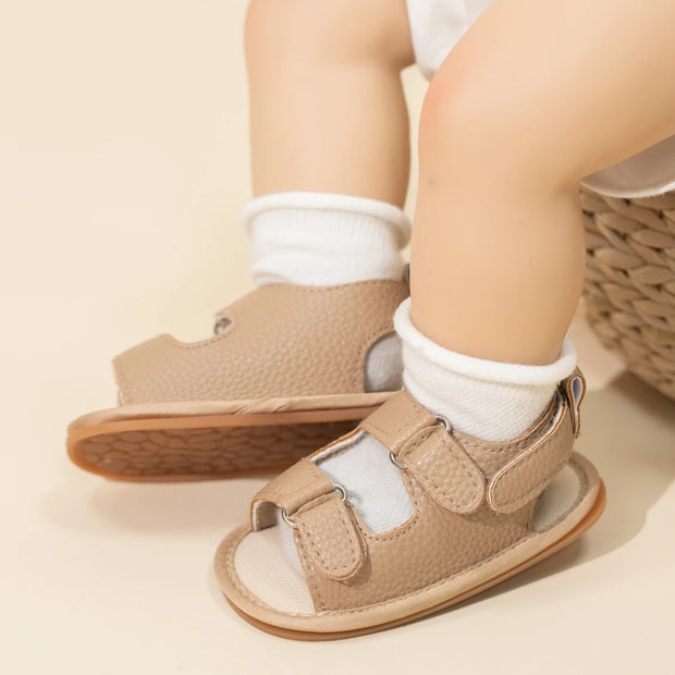 Baby's feet wearing brown sandals with white socks on a beige background