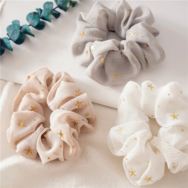 Three scrunchies in beige, gray, and white with star patterns on a light background.