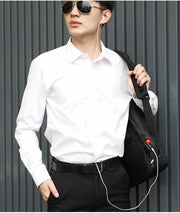 Man wearing a white shirt and black pants, holding a black bag with a red logo against a gray background.