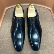 Pair of black dress shoes with gold accents on a textured surface