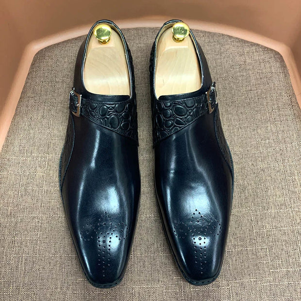 Pair of black dress shoes with gold accents on a textured surface