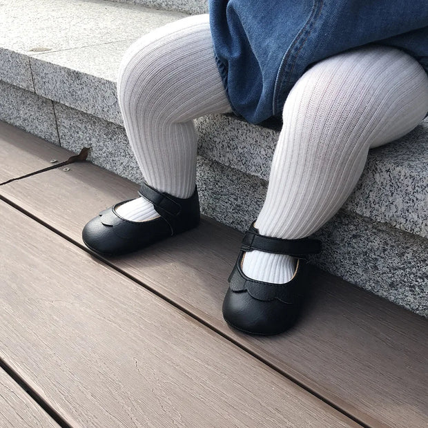 Person wearing black shoes and white socks sitting on a wooden deck.
