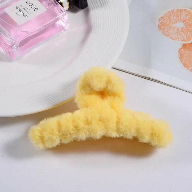 Yellow fluffy hanger on a white surface with a pink perfume bottle and a white hat in the background.
