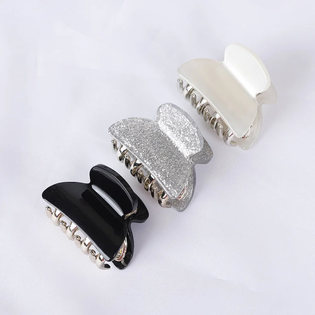Four hair clips in black, silver, and white on a light gray background