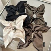 Set of four satin scrunchies in black, beige, and brown on a reflective surface.