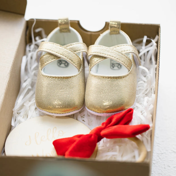 Gold baby shoes with a red bow in a box