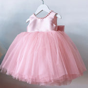 Pink children's dress with a bow on a hanger against a light gray background