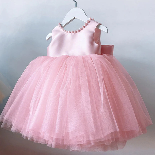 Pink children's dress with a bow on a hanger against a light gray background