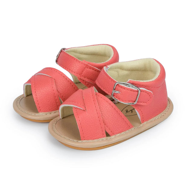 Pair of coral baby sandals with a buckle on a white background