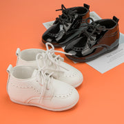 Pair of white baby shoes and black toddler shoes on an orange background