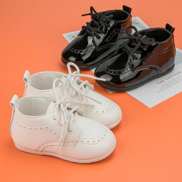 Pair of white baby shoes and black toddler shoes on an orange background