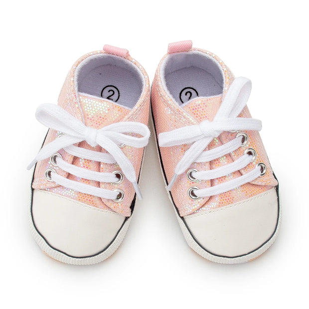 Pair of pink glittery baby sneakers with white laces on a white background