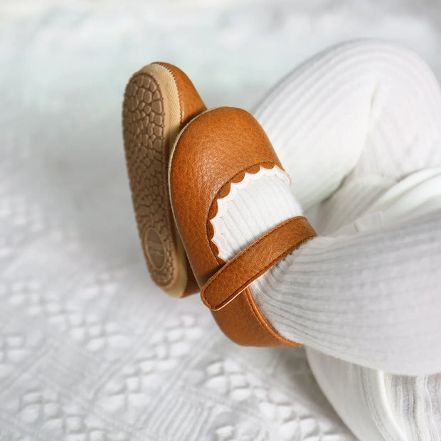 Brown leather baby shoes on a textured white surface