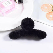 Black fluffy hair clip on a white surface with a pink product and orange slices in the background.