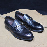 Pair of dark blue loafers with a gold buckle on a beige surface.