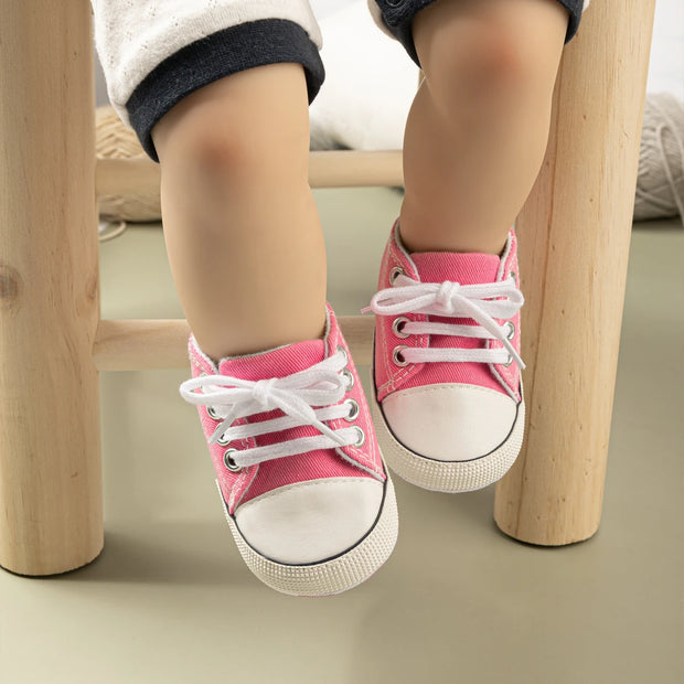 Child's feet wearing pink sneakers with white laces on a wooden stool.