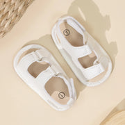 Pair of white baby sandals on a beige surface