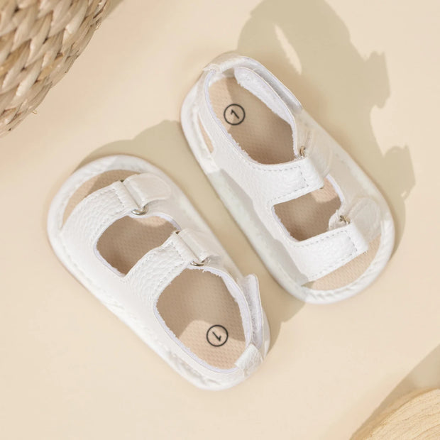 Pair of white baby sandals on a beige surface