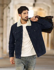 Man wearing a dark blue jacket with a white shirt and jeans, holding a brown leather bag.
