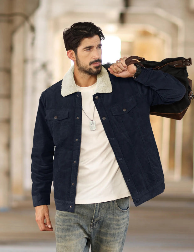 Man wearing a dark blue jacket with a white shirt and jeans, holding a brown leather bag.