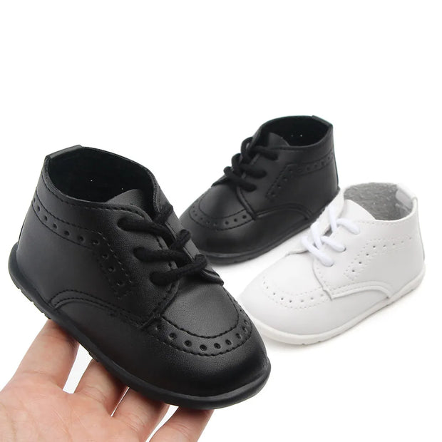 Black and white baby shoes held by a hand on a white background