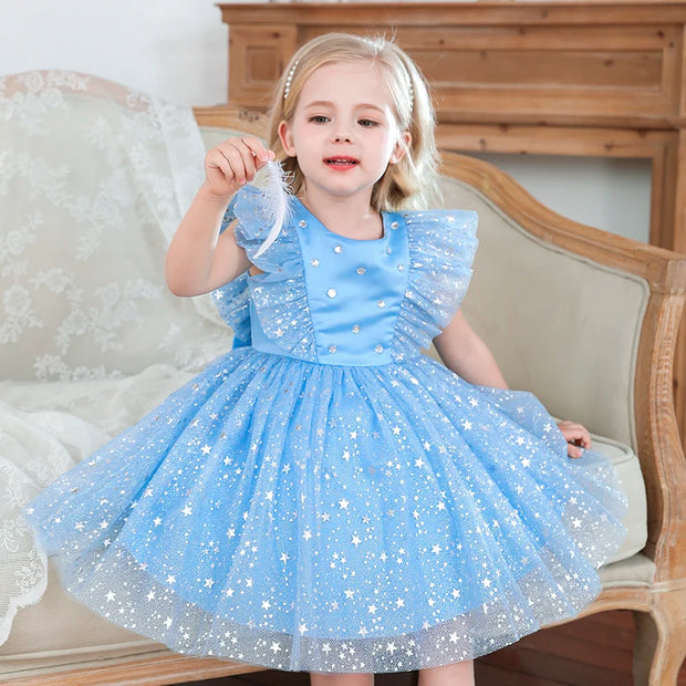 Young girl in a blue dress with star patterns sitting on a decorative chair.