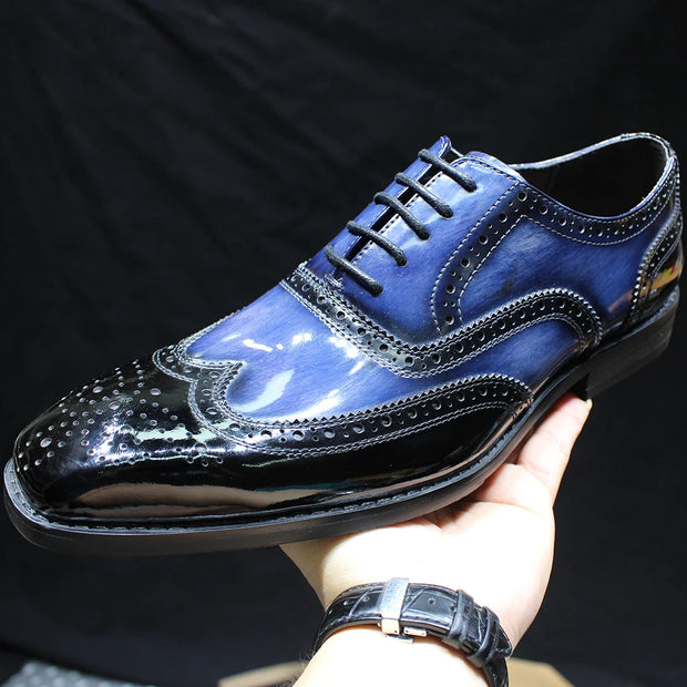 Blue leather dress shoe held by a hand against a dark background